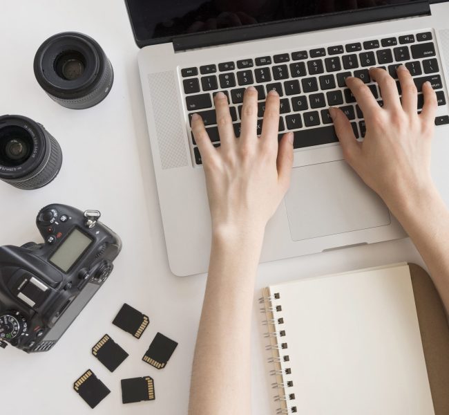 person-s-hand-typing-laptop-keyboard-with-camera-accessories-spiral-book